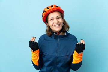 Young cyclist woman isolated on blue background making money gesture