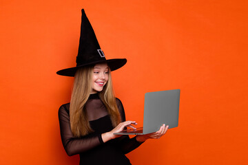 Photo of cheerful pretty lady wear black wizard costume cap chatting instagram twitter telegram facebook isolated orange color background