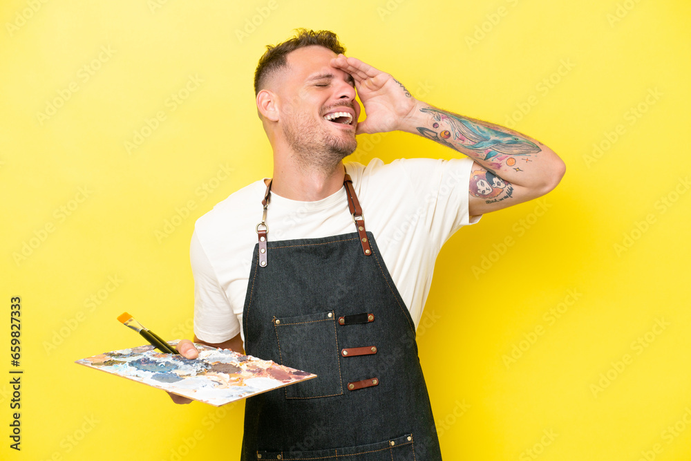 Wall mural Young artist caucasian man holding a palette isolated on yellow background smiling a lot