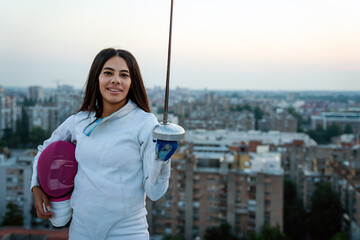 Portrait of young woman fencer wearing mask, white fencing costume and practicing outdoors.