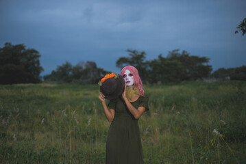 Young woman made up as a sad clown in a lonely field. Concept of loneliness and sadness. Halloween...