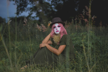 Young woman made up as a sad clown in a lonely field. Concept of loneliness and sadness. Halloween...