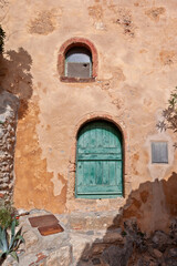 Fototapeta na wymiar Traditional house with ochre walls and wooden door and window, in the fortified town of Monemvasia, a castle-town of the byzantine era in the region of Laconia, in Peloponnese, Greece, Europe.