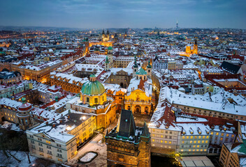 Beautiful winter dusk view of the illuminated old town of Prague, with snow covered roof tops and warm street light