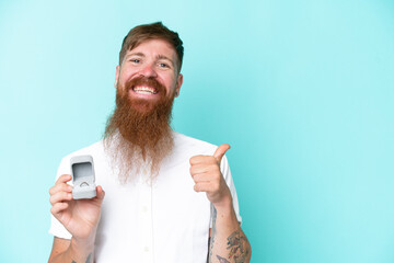 Redhead man with long beard holding a engagement ring isolated on blue background pointing to the...