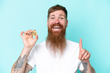 Redhead man with long beard holding a Bitcoin isolated on blue background pointing up a great idea
