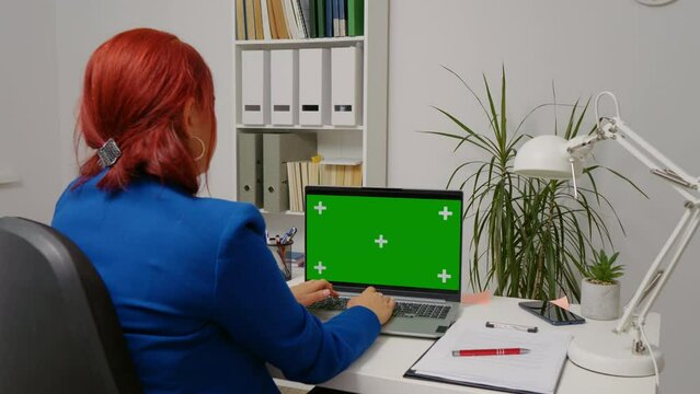 Business woman working in office interior on green screen laptop. Office person using laptop with green screen, sitting at table
