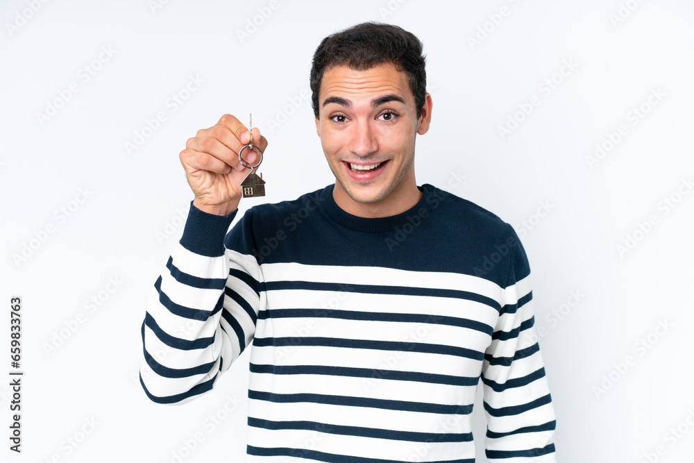 Wall mural Young caucasian man holding home keys isolated on white background with surprise and shocked facial expression