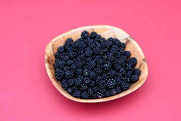 Freshly picked blackberries in a wooden bowl against a pink background, UK, Europe.
