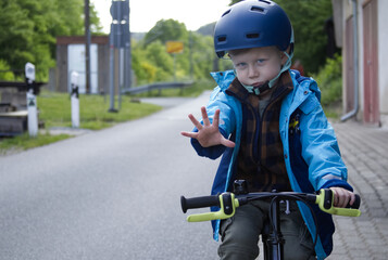 Naklejka premium A little boy on a bicycle extended his palm in front with a call to stop.