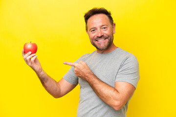 Middle age caucasian man with an apple isolated on yellow background and pointing it