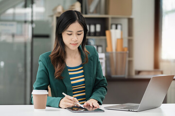 Businesswomen using tablet with laptop and document on desk in modern office.