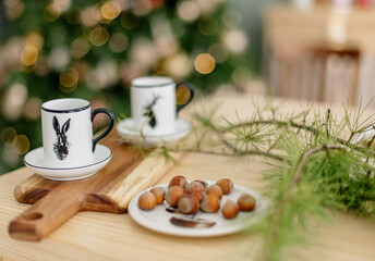 Christmas cups, nuts, fir on wooden kitchen with Christmas tree background
