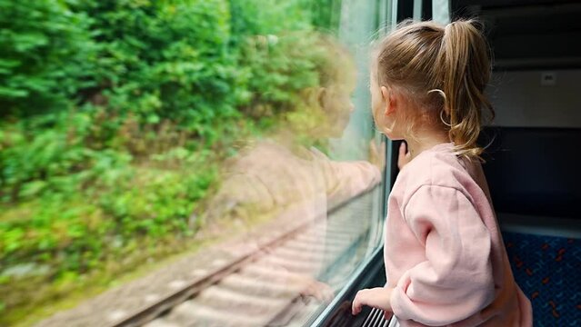 Cute little girl looking out train window outside, during moving. Traveling by railway, Europe