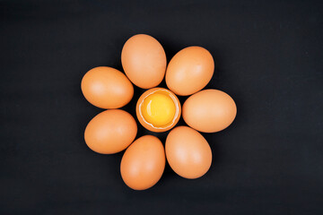 Top view of eggs with one chicken egg broken with yolk over black background