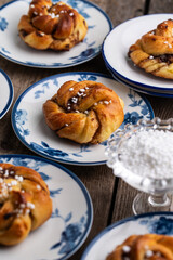 Homemade traditional Swedish cinnamon buns (swirls) on separate white and blue porcelain plates on wooden table.