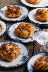 Homemade traditional Swedish cinnamon buns (swirls) on separate white and blue porcelain plates on wooden table.