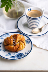 Homemade traditional Swedish cinnamon bun (swirl) on white and blue porcelain plate and cup of espresso coffee on white background.