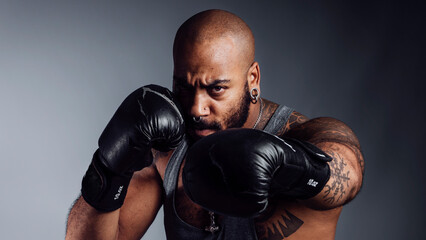 Portrait of a black man wearing boxing gloves performing a cross body look at the camera.