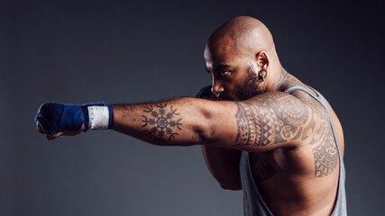 Mixed-race, muscular man with tattoos practicing boxing punches in the air in a studio shot