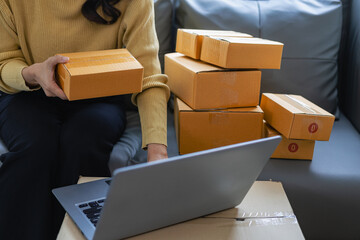 Beautiful Asian startup owner at home with laptop and package boxes in SME supply chain,...