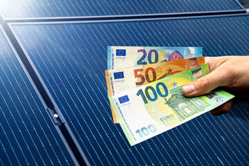 Euro bills held in a hand, with solar panels in the background