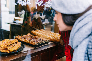 Two women wearing berets and warm clothes, looking at traditional pastries in a shop window