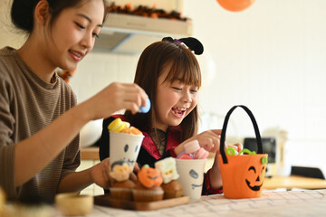 Smiling young mother and her little daughter getting ready for the holiday, making Halloween cupcakes