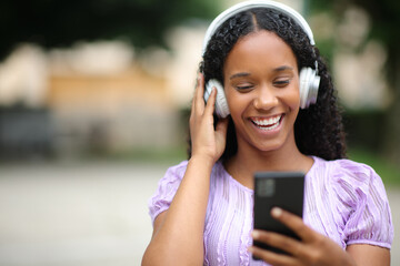 Happy black woman listening to music in the street