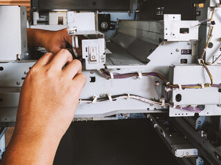A technician repairs a photocopier by dismantling machine and examining wires connected to power button and circuit board to determine cause of malfunction. - obrazy, fototapety, plakaty