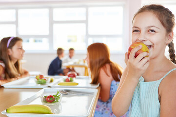 Happy girl eating apple in school cafeteria