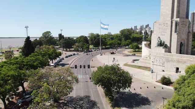 Drone sobre la ciudad de Rosario sobre la calle mientras se ve la bandera argentina y el monumento nacional a la bandera en dia soleado