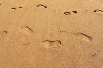 Fototapeta na wymiar Two sets of footprints on the sand one with slippers and one barefoot