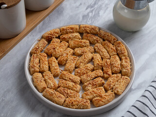 Kue Kastengel or Kaastangels are neatly presented on a white plate with attractive decorations. They are isolated against a kitchen background.