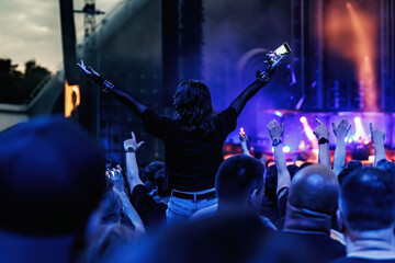 Stage lights against a happy woman with raised arms while enjoying a concert at a music festival