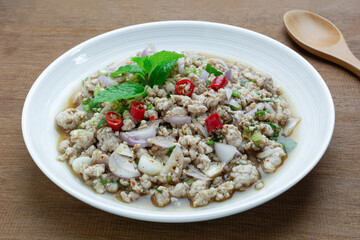 close up view of homemade style spicy minced pork salad in a ceramic dish on wooden table. popular local north eastern thailand food concept.