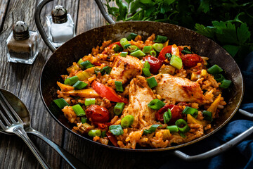 Jambalaya one pot dish - fried chicken breasts with white rice, tomatoes, bell pepper and celery on wooden table
