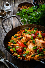 Jambalaya one pot dish - fried chicken breasts with white rice, tomatoes, bell pepper and celery on wooden table
