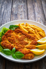 Crispy breaded seared chicken cutlet with French fries,   lemon and fresh vegetables on wooden table
