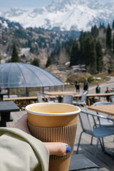 Hand holding orange fruit tea cup with the mountain background with copy space for your text. High quality vertical photo.