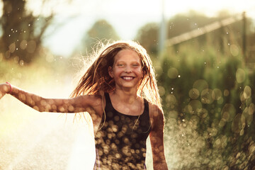 In the backyard of house, a young girl bursts with laughter and joy as she gleefully runs through a water sprinkler on a sunny summer day