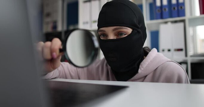Fraudster in balaclava holds magnifying glass and searches Internet for gullible users. Online scam concept