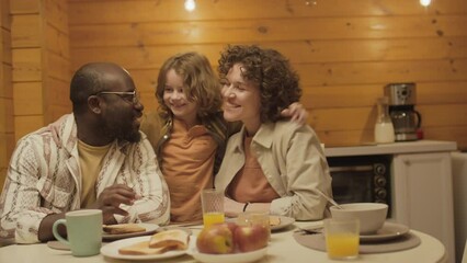 Medium shot of ethnically diverse couple sitting at dinner table talking while their child playing around - Powered by Adobe