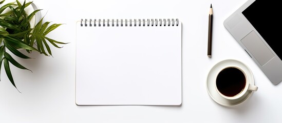Top down view of a contemporary white desk with laptop smartphone and supplies including a cup of coffee and a blank notebook page for writing With copyspace for text