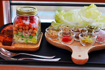 Salad in a Jar is layered with greens, with shredded carrots, chickpea, onion and tomato. Kept next to DIY thai Paan salad
