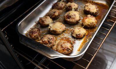 Parmesan stuffed mushrooms on a black background. Stuffed mushroom caps with cheese in a metal baking tray in the oven, selective focus