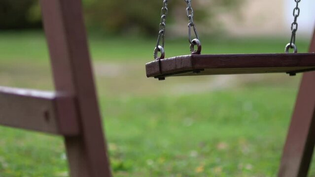 Close up of  empty wooden kids' swing moving in playground or backyard