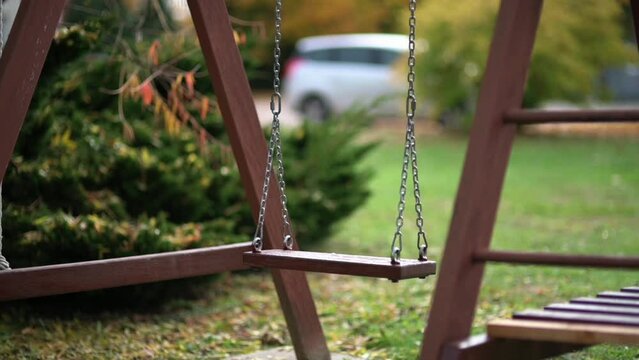 Empty wooden kids' swing moving in slow motion on playground or backyard