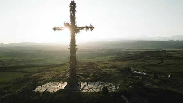 The largest iron cross in Armenia in the rays of the setting sun. On the background of high mountain Aragats in clear weather. Drone video. The camera approaches the cross and flies around it.