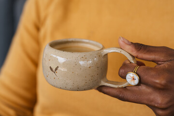 Closeup of female hands with a coffee mug of beverage. Beautiful dark skinned girl in pastel orange...